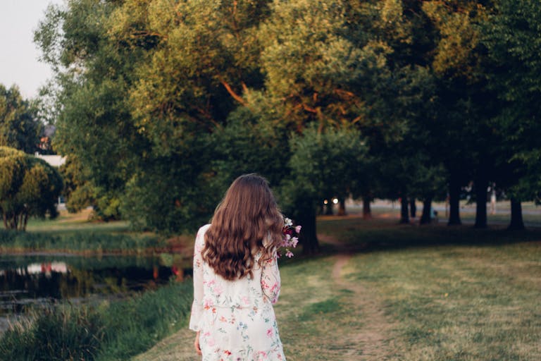 A woman in a floral dress walking along a path near a lake in a park.